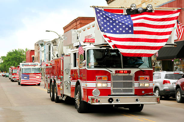Fire Trucks with American Flags at Small Town Parade A group of fire trucks with American flags on them drive down the road in a small town American Parade during a festival event. parade photos stock pictures, royalty-free photos & images