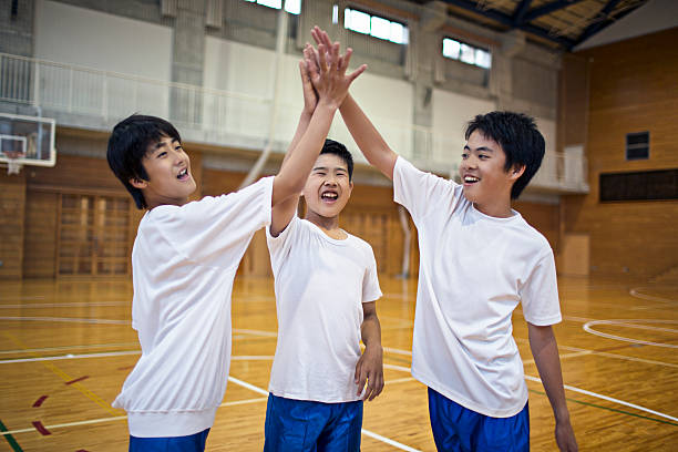 All for one Japanese  boys team in the school gymnasium celebrating they won the game. asian pe uniform stock pictures, royalty-free photos & images