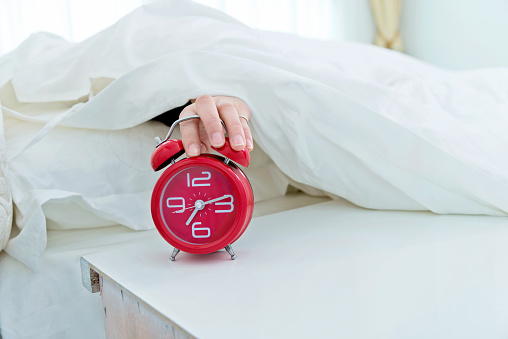 Beautiful asian woman hitting the alarm clock and turn off it.