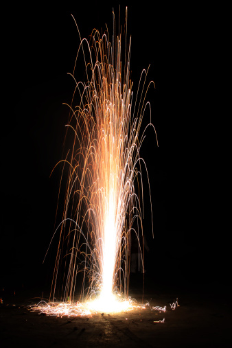 An empty cardboard box on a street corner is illuminated by an array of colorful fireworks, creating an eye-catching display