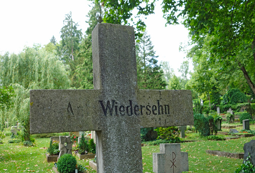 Stone Cross in graveyard with  words Auf wiedersehen Good bye