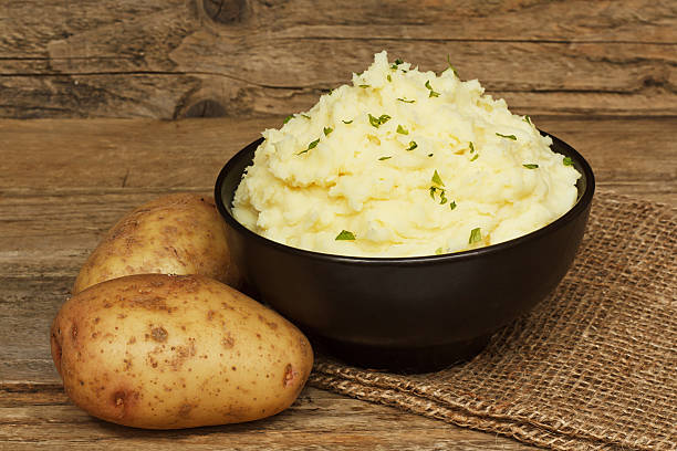 serving mashed potato serving of creamy mashed potato made from boiled potatoes mixed with butter and served in a black bowl on a traditional rustic background mashed potatoes stock pictures, royalty-free photos & images