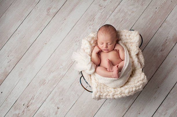Newborn Baby Sleeping in a Wire Basket A portrait of a seven day old, newborn baby sleeping in a wire basket on a whitewashed, wooden floor. gender neutral photos stock pictures, royalty-free photos & images