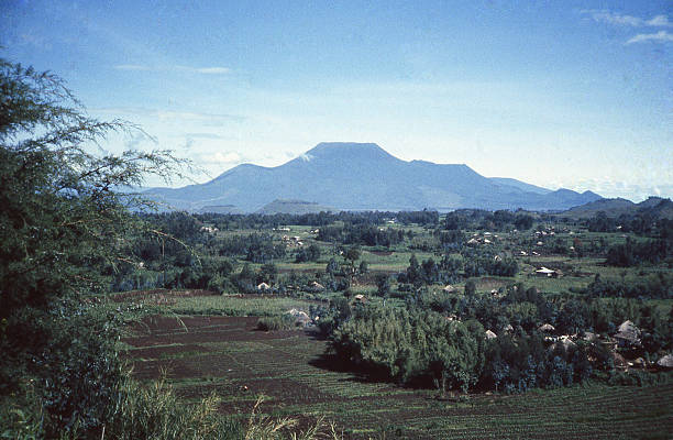 Mid-1980s view of Nyiragongo Volcano's Silhouette on the Zaire (Democratic Republic of Conto) side of the border and traditional village huts seen on the Mudende Rwanda side of the border