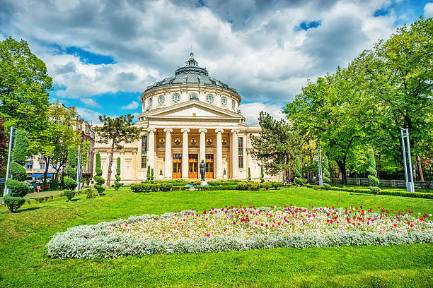 Romanian Athenaeum Of Bucarest, Romania Romanian Athenaeum is Bucharest's most prestigious concert hall and one of the most beautiful buildings in the city. Beautiful green trees and flowers in park in front of the building. Bucarest, Romania bucharest stock pictures, royalty-free photos & images
