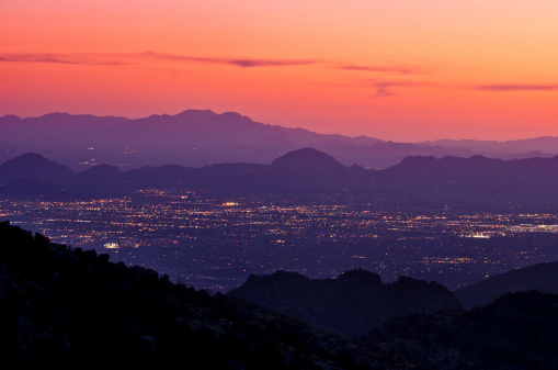 Tucson's city lights at dusk with the mountains in the foreground and in the distance.