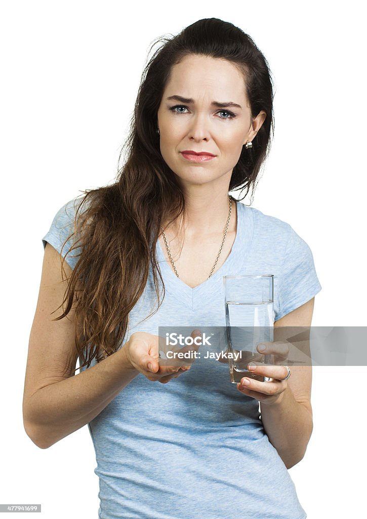 Woman about to take pills. An unhappy woman in pain holding glass of water and pain killer pill, looking at camera. Isolated on white. Birth Control Pill Stock Photo