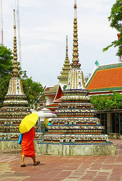 Buddhist monk dressed in vibrant colors walks in a temple of Bangkok