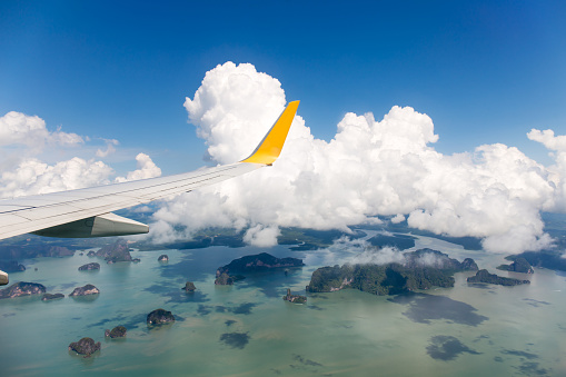 Wing of the plane with blue sky and cloud over island sea