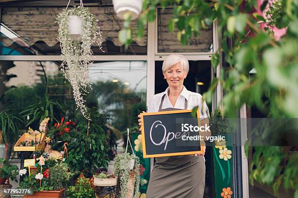 Smiling Mature Woman Holding Open Sign At Flower Shop Stock Photo - Download Image Now