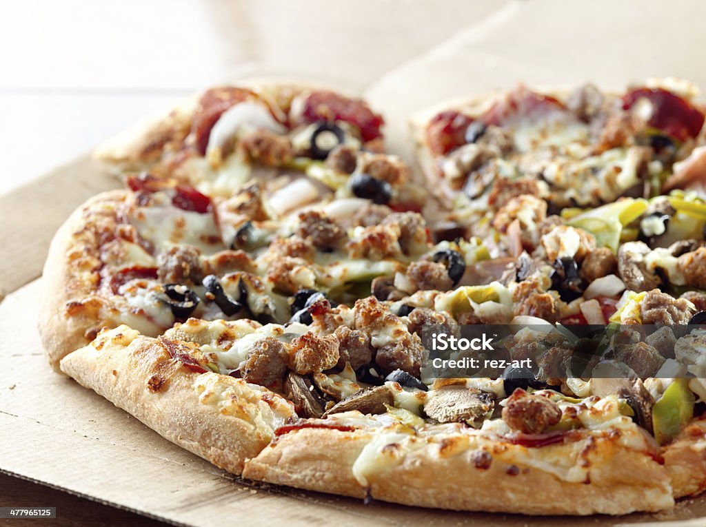 pizza sitting on cardboard box supreme pizza sitting on card board box with italian sausage, peppers, black olives, mushrooms, and pepperoni. Italian Culture Stock Photo