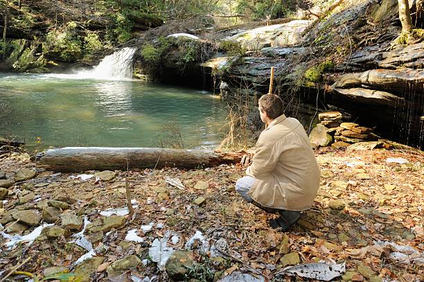 istock Man crouched near waterfall in woods 477970201