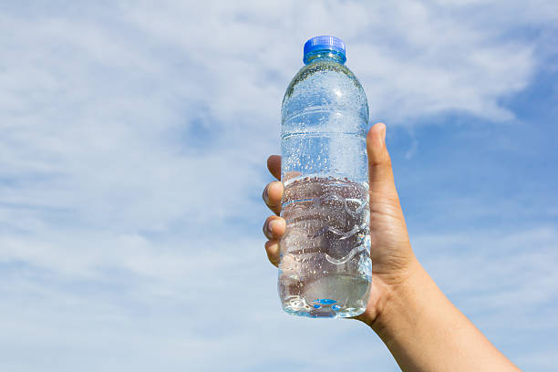 istock hand holding water bottle on sky background 477973454