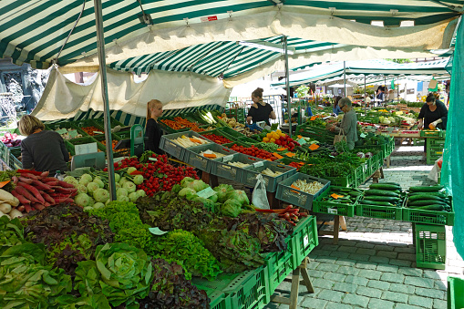 Tübingen, Germany - June 17, 2015: View of a huge vegetable and fruits stand on the market square. Three sales women on the left and two customers on the right side to be seen. Some more people and stands in the background. 