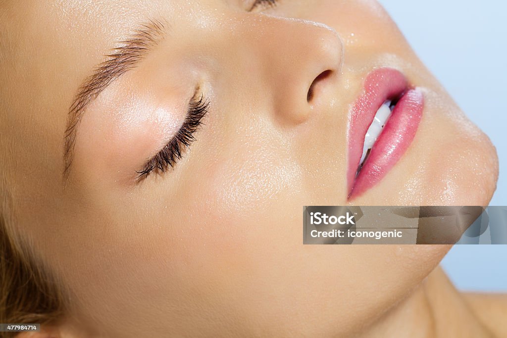 Summer Beauty Closeup of beautiful smooth young dewy skin with water drops over sky blue background. Serene woman with eyes closed in summer sun. Dew Stock Photo