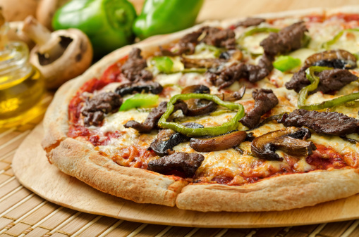 A delicious steak and mushroom pizza with green peppers and olive oil.