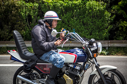 Fujisawa, Japan - May 9, 2015: Japanese biker with vintage motorbikes driving in the motorway and eating an icecream.