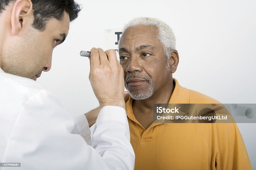 Male Doctor Testing Patient's Eye In Clinic Mature male doctor testing an African American patient's eye in clinic Eye Exam Stock Photo