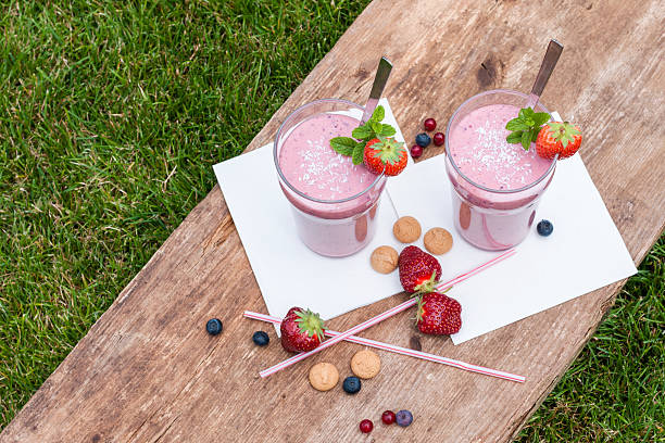 Fruity berry milkshake outdoors 2 glasses with a berry milkshake and decoration on an old wooden board lying on grass, landscape, top view yogurt fruit biscotti berry fruit stock pictures, royalty-free photos & images