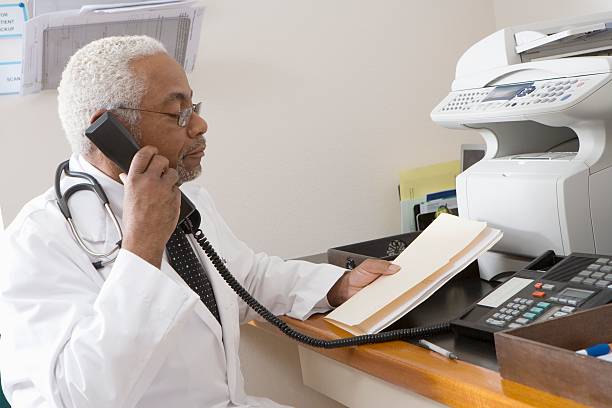 African American senior male doctor holding document while using phone stock photo