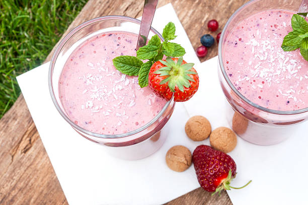 Fruity berry milkshake outdoors 2 glasses with a berry milkshake and decoration on an old wooden board lying on grass, landscape, top view yogurt fruit biscotti berry fruit stock pictures, royalty-free photos & images