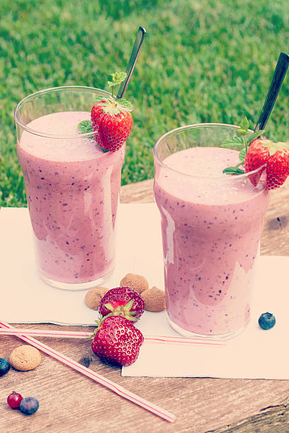 Fruity berry milkshake outdoors 2 glasses with a berry milkshake and decoration on an old wooden board lying on grass, portrait format with Instagramm effect yogurt fruit biscotti berry fruit stock pictures, royalty-free photos & images