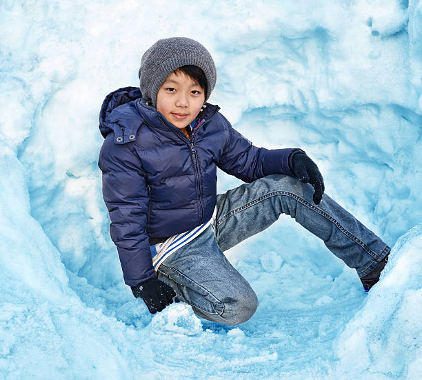 Portrait of smiling cute teenage boy, preteen playing in snow, in a snow-covered hat  in winter nature. Brown coat
