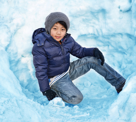 Active young Asian boy wearing jeans and winter hat in winter snow.