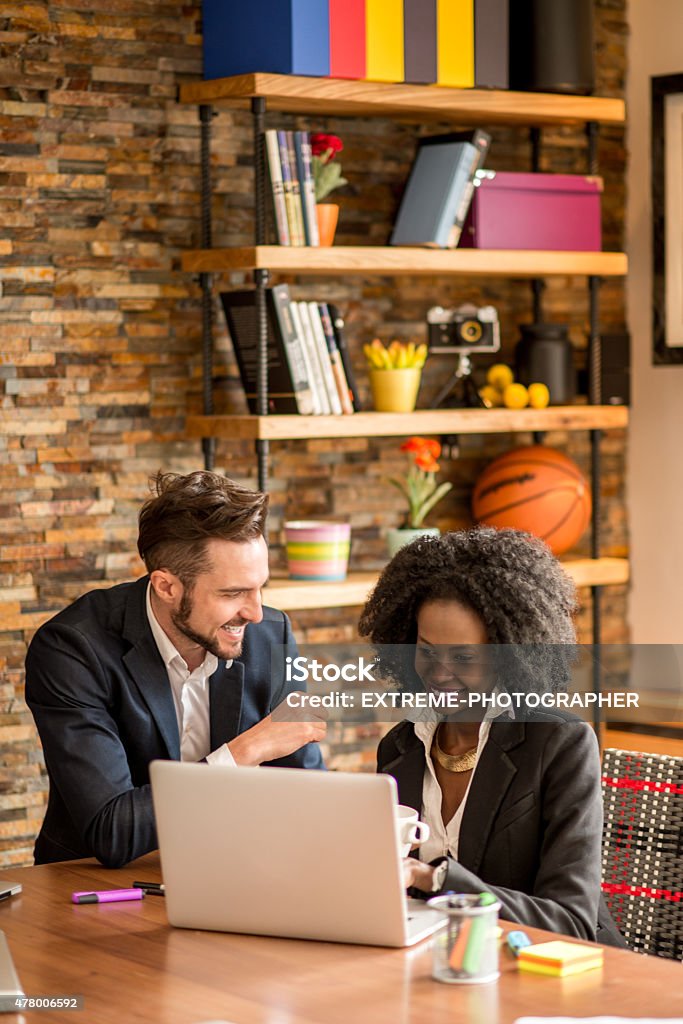 Coworkers in the office Caucasian male and black female colleagues working in the office. They are havig a conversation while woman works on her laptop and holding a cup of coffee. 2015 Stock Photo