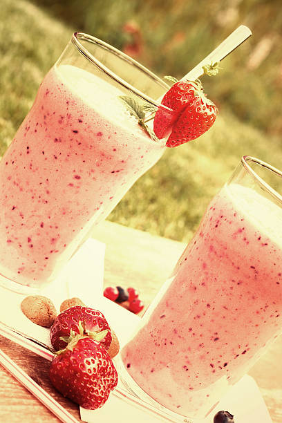 Fruity berry milkshake outdoors 2 glasses with a berry milkshake and decoration on an old wooden board lying on grass, portrait format with Instagramm effect, oblique yogurt fruit biscotti berry fruit stock pictures, royalty-free photos & images
