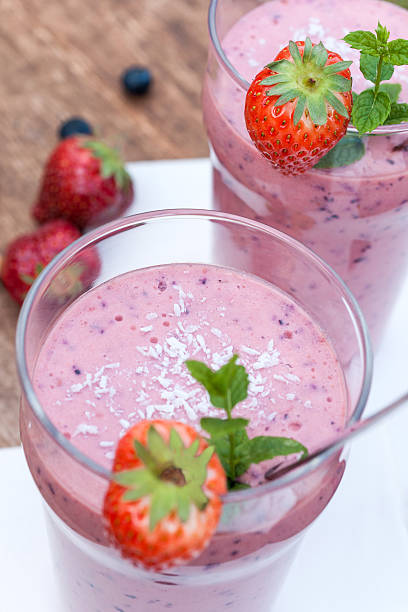 Fruity berry milkshake outdoors 2 glasses with a berry milkshake and decoration on an old wooden board,  glasses only partially visible, portrait format yogurt fruit biscotti berry fruit stock pictures, royalty-free photos & images