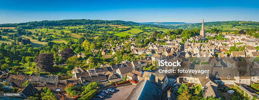 Aerial panorama over idyllic country village cottages green summer fields Clear blue summer skies and vibrant green patchwork fields above the iconic Cotswold village of Painswick, with its honey coloured limestone cottages and historic church spire, Gloucestershire, UK. ProPhoto RGB profile for maximum color fidelity and gamut. Cotswolds Stock Photo