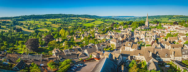 Aerial panorama over idyllic country village cottages green summer fields Clear blue summer skies and vibrant green patchwork fields above the iconic Cotswold village of Painswick, with its honey coloured limestone cottages and historic church spire, Gloucestershire, UK. ProPhoto RGB profile for maximum color fidelity and gamut. gloucestershire stock pictures, royalty-free photos & images