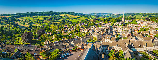 Aerial panorama over idyllic country village cottages green summer fields Clear blue summer skies and vibrant green patchwork fields above the iconic Cotswold village of Painswick, with its honey coloured limestone cottages and historic church spire, Gloucestershire, UK. ProPhoto RGB profile for maximum color fidelity and gamut. house uk countryside stock pictures, royalty-free photos & images