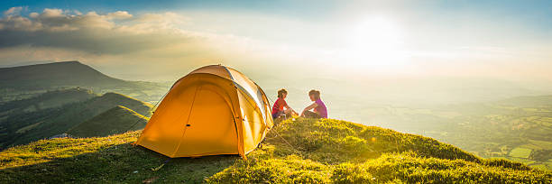 Children tent camping on idyllic summer sunset mountain top panorama Kids in colorful outdoor clothing sitting beside a bright yellow dome tent camped in an idyllic mountain top meadow illuminated by the warm light of a summer sunset. ProPhoto RGB profile for maximum color fidelity and gamut. family camping stock pictures, royalty-free photos & images