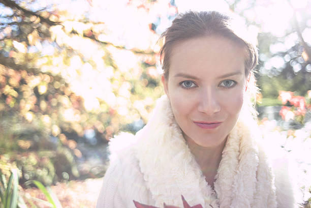 A portrait of a beautiful woman in white, standing in front of out of focus autumn background with bokeh