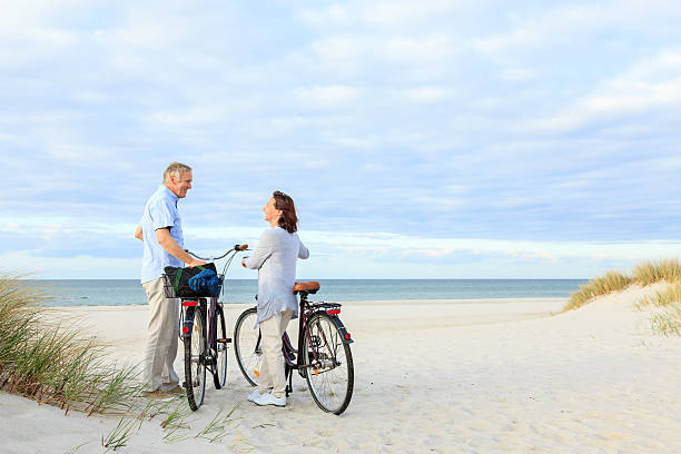 matura coppia all'aperto sulla spiaggia - mature adult bicycle senior adult heterosexual couple foto e immagini stock