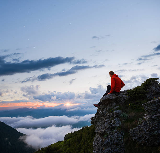istock Man sitting on a rock admiring the cloudy mountain landscape 478012982