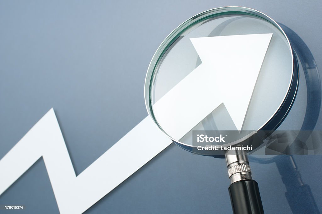 Looking upside growth arrow with magnifying glass. Concept image White arrow and magnifying glass on dark blue background. 2015 Stock Photo