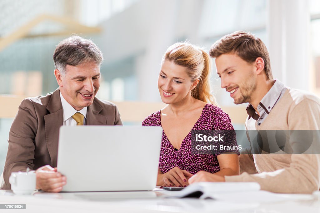 Young happy couple on a meeting with financial advisor. Young happy couple having a meeting with their insurance agent. They are using computer and talking. 2015 Stock Photo