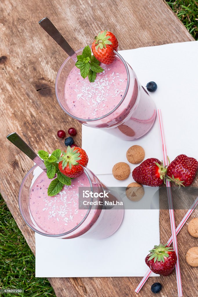 Fruity berry milkshake outdoors 2 glasses with a berry milkshake and decoration on an old wooden board lying on grass, portrait format, top view 2015 Stock Photo