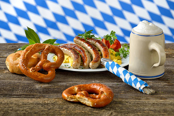 Bavarian lunch Fried Bavarian sausages on potato salad served with pretzels and half a liter of Bavarian beer in a tankard, in the background the white-blue flag of Bavaria oktoberfest food stock pictures, royalty-free photos & images