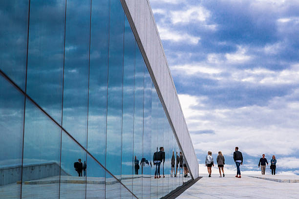 Oslo, Norway - June 13, 2015: The modern Opera House in Oslo, Norway. People are walking up the slope and onto the roof, and they are reflected in the glass windows.
