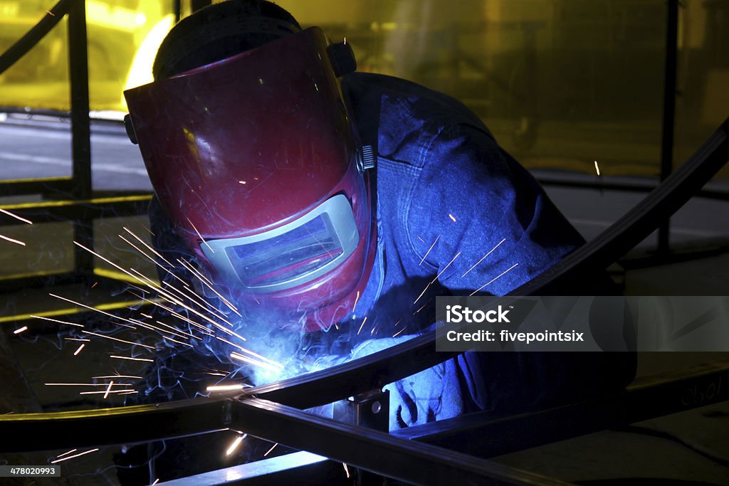 welding in a factory man with red protective mask on welding some steel Burning Stock Photo