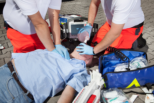 Medical emergency. Two male paramedics treating an unconscious victim on the street - performing a cardiopulmonary resuscitation (CPR). Various medical equipment.