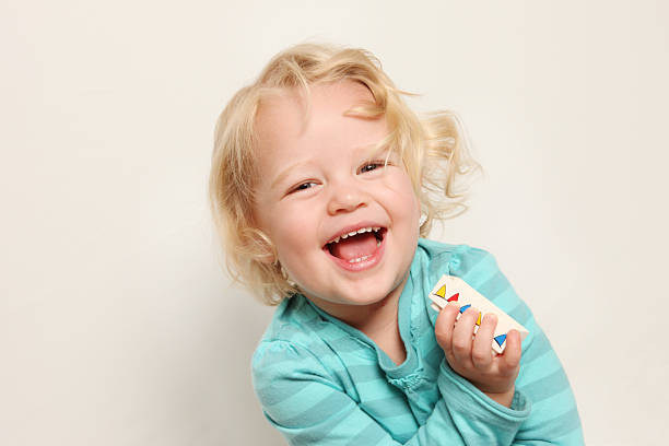 Blond Girl Laughing taken against a beige background A blond girl laughing and holding onto a building brick.  Taken against a beige background in a studio.  The cute little girl is wearing a blue striped t-shirt, has wavy hair and is laughing out loud. child laughing hysterically stock pictures, royalty-free photos & images