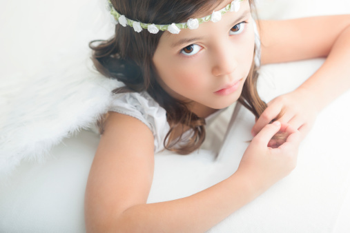 A red-haired little girl in a green T-shirt lies on a white bed at home and smiles. Portrait of a five year old girl.