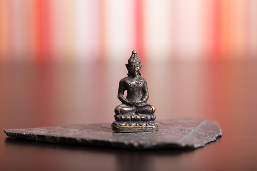 Tiny Statue of Buddha in the Lotus Position over a small rock platform on top of a wooden table