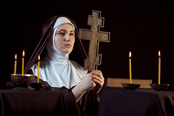 Nun with cross Young catholic nun is praying. Orthodox cross in her hands. Photo on black background. nun catholicism sister praying stock pictures, royalty-free photos & images