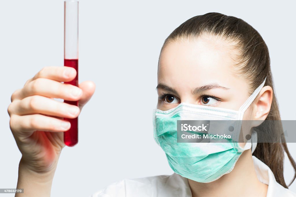 Girl in a mask holding test tube with red liquid Image of a beautiful young girl in doctors mask holding a test tube with red liquid - science and medicine concept 2015 Stock Photo